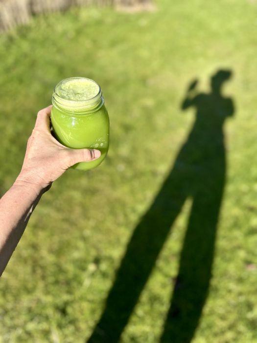Un bocal de jus vert tenu à bout de bras, au soleil sur l'herbe