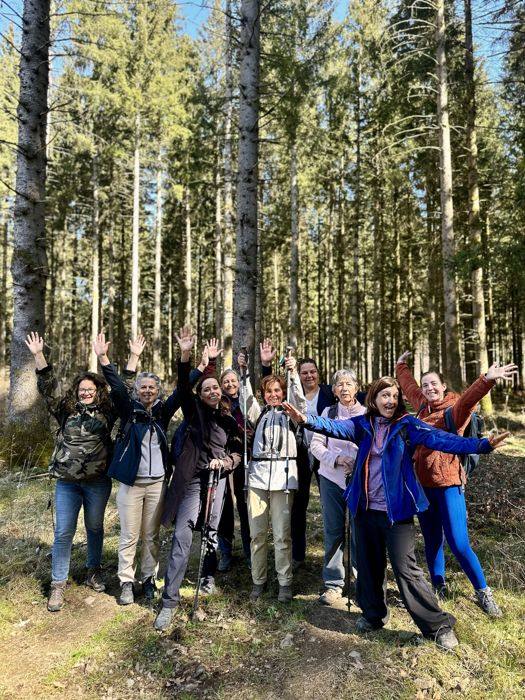 Groupe de randonneuses joyeuses, bras levés, dans une forêt de sapins