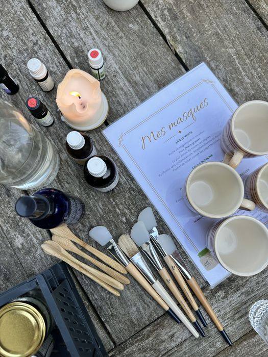 Atelier masques à l'argile : pinceaux, huiles essentielles et bols sur une table en bois