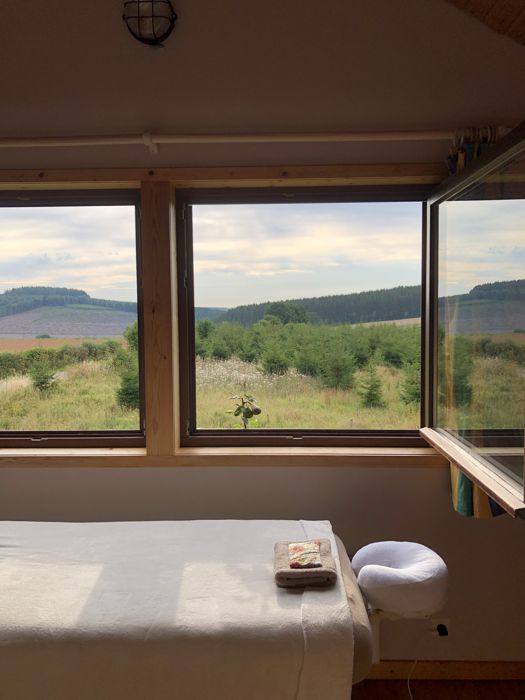 Table de massage devant de grandes fenêtres ouvertes sur la nature
